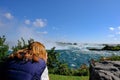 Ginger-haired woman seen aiming her camera at the famous Niagara Falls, Ontario, Canada.