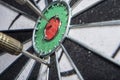 background in soft focus with a darts board with a closeup of an arrow hitting the center and an opponent`s arrow stuck nearby