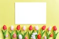 Background with tulips and Easter eggs on a yellow background with a white sheet of paper. Royalty Free Stock Photo