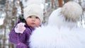 on the background of the winter forest, a portrait of a small one-year-old girl in a funny hat with a bumbon. the girl