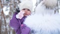 On the background of the winter forest, a portrait of a small one-year-old girl in a funny hat with a bumbon. the girl