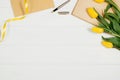 Background with yellow tulips, blank notepad on white wooden table