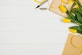 Background with yellow tulips, blank notepad on white wooden table