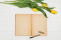 Background with yellow tulips, blank notepad on white wooden table