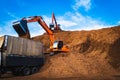 Backhoe standing on big pile of wood chips loading up into truck. Woodchips raw material storing and transportation.