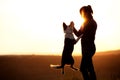Backlight Silhouette of a woman with her jumping dog, playing on