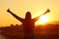 Backlight of a woman raising arms with thumbs up