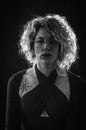 Backlit black and white close up portrait of a curly blonde woman with eyeglasses looking to the side a little sad