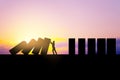 Backlit businessman stopping abstract wooden domino blocks on bright sunset sky background with mock up place. Crisis, recession