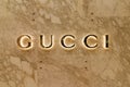 Backlit gold Gucci brand logo on tan marble wall