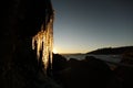 Backlit icicles on rocky shore by the ocean at sunset