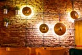 Backlit illuminated cymbals plates ornamenting a brick wall, with green artificial flowers hanging in pots and wooden chair tops. Royalty Free Stock Photo