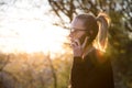 Backlit rear view of young woman talking on cell phone outdoors in park at sunset. Girl holding mobile phone, using Royalty Free Stock Photo