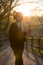 Backlit rear view of young woman talking on cell phone outdoors in park at sunset. Girl holding mobile phone, using Royalty Free Stock Photo