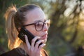 Backlit rear view of young woman talking on cell phone outdoors in park at sunset. Girl holding mobile phone, using Royalty Free Stock Photo