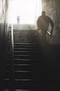Backlit staircase in an underground passage during rainfall with two figures ascending into bright light Royalty Free Stock Photo