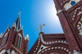 Backlit white cross with ornate Gothic Revival architecture church, blue sky with sun glow