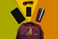 Backpack with accessories, tablet computer, phone, glasses and a thermo mug on a bright background. Outfit of student, teenager, y