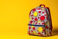 Backpack with colorful dots against a bright yellow background captured in a studio setting Royalty Free Stock Photo