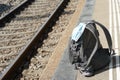 Backpack with a n95 face mask attached on it, on a train station platform with rails in the background, transport at coronavirus Royalty Free Stock Photo