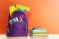 Backpack with school stationery on wooden table against orange background, space for text Royalty Free Stock Photo