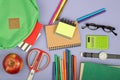 Backpack and school supplies notepad, felt-tip pens, eyeglasses, scissors, calculator, book, watch on blue paper background