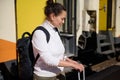 Backpacked female tourist holding suitcase, standing on the train station platform against the colorful train background