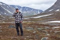 Backpacker calling with mobile phone in highland of mountains. Full-length man standing in tundra, copy space