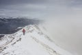 Backpacker climbing a mountain narrow snowy ridge in winter Royalty Free Stock Photo