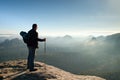 Backpacker with eyeglasses and poles in hand. Sunny day in rocky mountains. Hiker with big backpack on rocky view point above mist Royalty Free Stock Photo