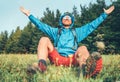 Backpacker man has a rest break enjoying mountain landscape wide opened and raised arms. He wears in blue rain coat poncho and