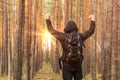 Backpacker traveler with backpack raised his hands up. Survival scene in the forest. Sunrise in pine forest. Copy space.