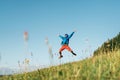 Backpacker traveler emotionally jumping over green grass mountain meadow with backpack with wide opened arms and legs. Human`s
