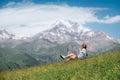 Backpacker woman sitting on a green grass hill and enjoying snowy slopes of Kazbek 5054m mountain with a backpack while she Royalty Free Stock Photo