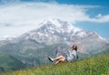 Backpacker woman sitting on a green grass hill and enjoying snowy slopes of Kazbek 5054m mountain with a backpack while she Royalty Free Stock Photo