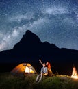 Backpackers girl and guy looking at the shines starry sky at night. Young couple sitting near tent and campfire Royalty Free Stock Photo