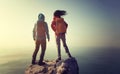 Backpackers stand on sunrise seaside mountain top rock edge