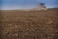 backside distant cultivator raises great dust on ploughed soil