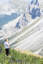 Backside girl admires, on a flowery meadow, the mountains that are part of the Dolomites, Eur