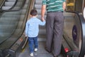 Backside of Little Asian 3 years old toddler boy child and dad holding hands on moving escalator at department store, Father and