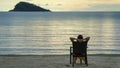 Backside shot of woman sitting on the chair and enjoying on the beach.