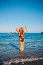 Backside view of bikini woman in Santa hat holding hand up standing in the sea