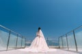Backside view of bride stands on balcony in white dress with long train Royalty Free Stock Photo