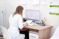 Backside view of caucasian blonde woman doctor in white uniform in clinic hospital works on computer. Cabinet and other Royalty Free Stock Photo