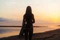 Backside view silhouette of surfer girl with surf board on beach at sunset Royalty Free Stock Photo