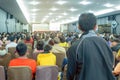 Backside view of spectators standing in a gathering in the back of auditorium full of people.