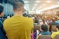 Backside view of spectators standing in a gathering in the back of auditorium full of people.