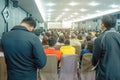 Backside view of spectators standing in a gathering in the back of auditorium full of people.