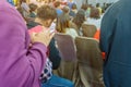 Backside view of spectators standing in a gathering in the back of auditorium full of people.