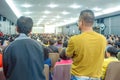 Backside view of spectators standing in a gathering in the back of auditorium full of people.